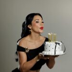 Elegant woman blowing out candles on a stylish birthday cake.